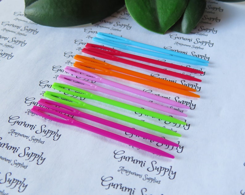 May include: A set of ten colorful plastic crochet hooks, arranged in a rainbow pattern. The hooks are labeled "Gurumi Supply" and are designed for amigurumi projects.