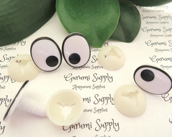 Puede incluir: Dos pares de ojos saltones de plástico blanco con pupilas negras y cuatro cuencas de ojos de plástico blanco. Las cuencas de los ojos tienen un pequeño agujero en el centro. La imagen tiene el texto "Gurumi Supply Amigurumi Supplies" impreso en el fondo blanco.