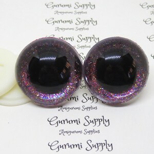 May include: Two black and purple glitter safety eyes with a black pupil. The eyes are 12mm in diameter and have a flat back.