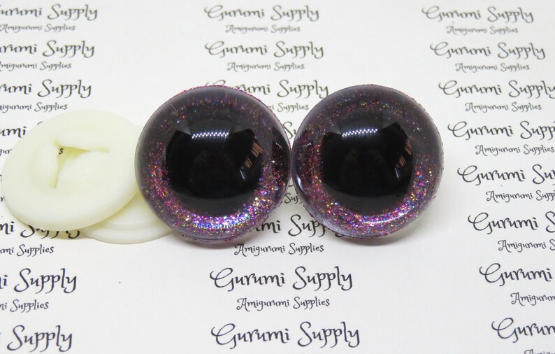 May include: Two black and purple glitter safety eyes with a black pupil. The eyes are 12mm in diameter and have a flat back.