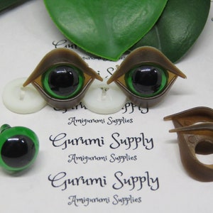 May include: A collection of amigurumi supplies, including two brown and green doll eyes with black pupils, a single green eye, and two brown eye frames. The text "Gurumi Supply" and "Amigurumi Supplies" is visible.