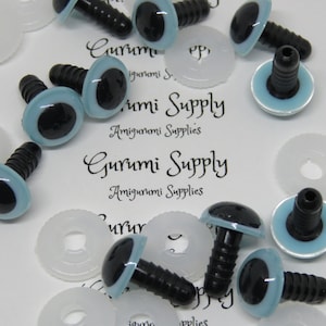 May include: A close-up of a group of blue and black plastic safety eyes with black plastic washers. The eyes are on a white surface with the text "Gurumi Supply Amigurumi Supplies" printed on it.