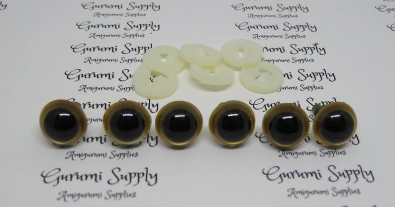Puede incluir: Seis ojos de seguridad de pl&aacute;stico con borde dorado y pupilas negras. Los ojos est&aacute;n dispuestos en dos filas de tres. Los ojos est&aacute;n sobre un fondo blanco con el texto "Gurumi Supply" impreso en el fondo.