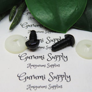 May include: Two black plastic safety eyes with a screw back, and two white plastic washers. The eyes are on a white surface with the text "Gurumi Supply Amigurumi Supplies" printed on it.