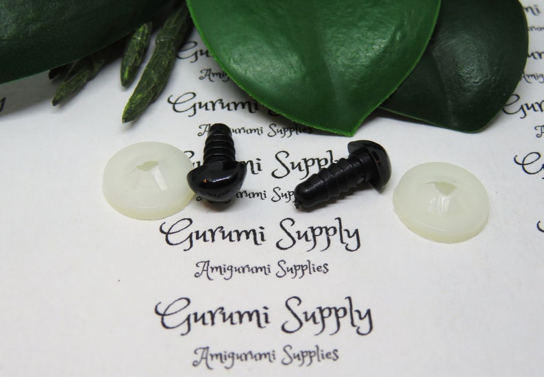 May include: Two black plastic safety eyes with a screw back, and two white plastic washers. The eyes are on a white surface with the text "Gurumi Supply Amigurumi Supplies" printed on it.
