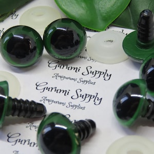 Op de afbeelding: Zes groene plastic veiligheidsogen met zwarte pupillen en een schroefrug. De ogen liggen op een wit oppervlak met de tekst "Gurumi Supply Amigurumi Supplies" erop gedrukt.
