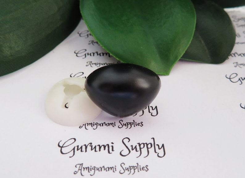 May include: Two plastic safety eyes for amigurumi projects. One eye is black and the other is white. The eyes are on a white surface with the text "Gurumi Supply" printed on it.