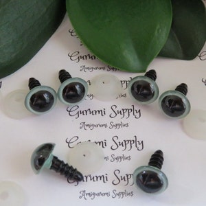 Könnte beinhalten: Sechs schwarze Sicherheitsaugen mit silbernem Schraubverschluss und einer transparenten Kunststoffscheibe. Die Augen liegen auf einer weißen Oberfläche mit dem aufgedruckten Text "Gurumi Supply Amigurumi Supplies".