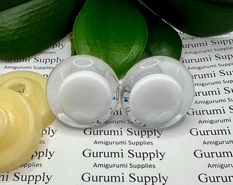 May include: Two white glass eyes for amigurumi projects. The eyes are clear with a white pupil and are sitting on a white background with the text "Gurumi Supply Amigurumi Supplies" repeated multiple times.