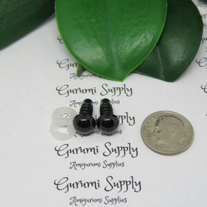 May include: Two black plastic safety eyes with a white plastic washer, a silver dime for size comparison, and the text "Gurumi Supply Amigurumi Supplies" printed on a white background.