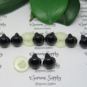 May include: A close-up of six black plastic safety eyes with white plastic washers. The eyes are for use in amigurumi and other crafts.