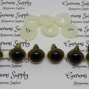 Puede incluir: Seis ojos de seguridad marrones con pupilas negras y detalles en metal dorado. Los ojos est&aacute;n dispuestos en dos filas de tres. Los ojos est&aacute;n sobre un fondo blanco con el texto "Gurumi Supply Amigurumi Supplies" impreso en el fondo.