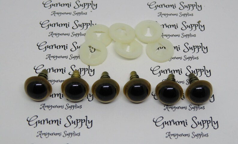 Puede incluir: Seis ojos de seguridad marrones con pupilas negras y detalles en metal dorado. Los ojos est&aacute;n dispuestos en dos filas de tres. Los ojos est&aacute;n sobre un fondo blanco con el texto "Gurumi Supply Amigurumi Supplies" impreso en el fondo.