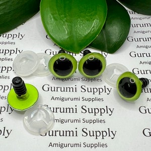 May include: Four green safety eyes with black pupils and a white ring around the pupil. The eyes are on a white background with the text "Gurumi Supply" and "Amigurumi Supplies".