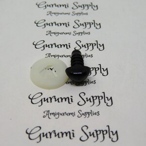 May include: A close-up of a black plastic safety eye for amigurumi projects. The eye is attached to a white plastic washer. The image is on a white background with the text "Gurumi Supply Amigurumi Supplies" printed on it.