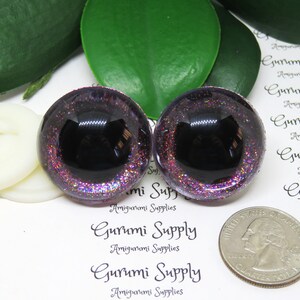 May include: Two purple glitter safety eyes with black pupils. The eyes are approximately the size of a US quarter.