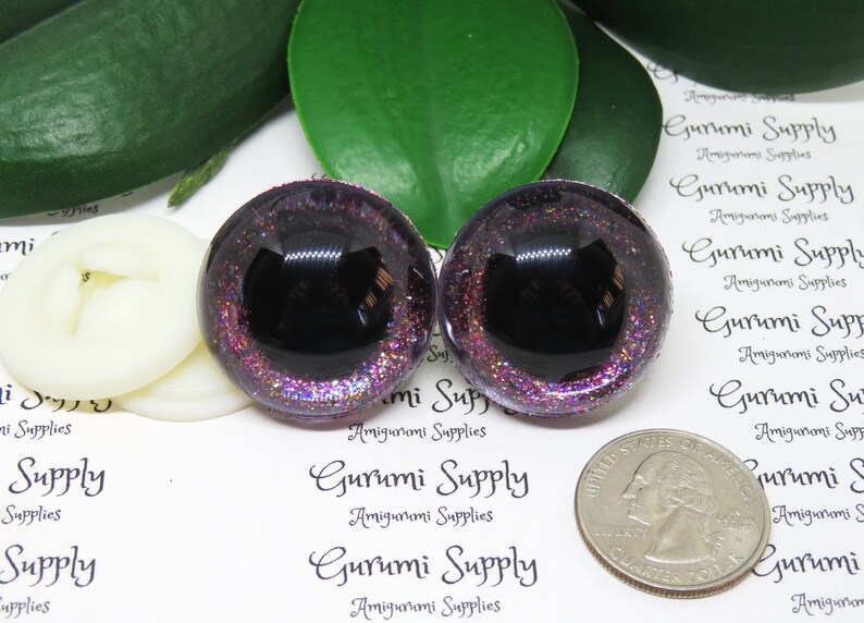 May include: Two purple glitter safety eyes with black pupils. The eyes are approximately the size of a US quarter.