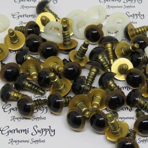 Puede incluir: Primer plano de un mont&oacute;n de ojos de seguridad de pl&aacute;stico negro y marr&oacute;n con tornillos de metal dorado. Los ojos se utilizan para amigurumi y otros proyectos de artesan&iacute;a.