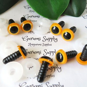 May include: Six orange and black plastic safety eyes with black plastic screw backs. The eyes are 12mm in diameter. The eyes are on a white surface with the text "Gurumi Supply Amigurumi Supplies" printed on it.