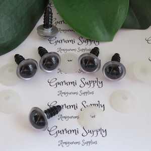 May include: Six black safety eyes with silver washers and black screw posts. The eyes are on a white background with the text "Gurumi Supply Amigurumi Supplies" repeated multiple times.