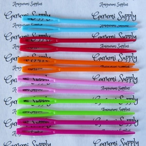 May include: A set of ten colorful plastic crochet hooks, each with a different color: light blue, blue, red, orange, pink, lime green, green, magenta, and pink. The hooks are labeled "Gurumi Supply" and "Amigurumi Supplies".