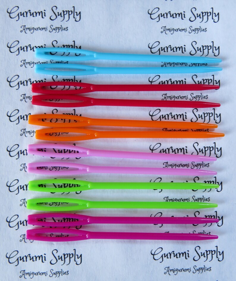 May include: A set of ten colorful plastic crochet hooks, each with a different color: light blue, blue, red, orange, pink, lime green, green, magenta, and pink. The hooks are labeled "Gurumi Supply" and "Amigurumi Supplies".