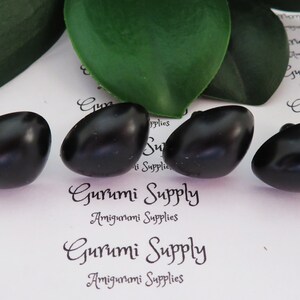 May include: Four black plastic safety eyes for amigurumi projects. The eyes are oval shaped and have a glossy finish. The eyes are on a white background with the text "Gurumi Supply Amigurumi Supplies" printed on it.