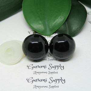 May include: Two black plastic safety eyes for amigurumi projects. The eyes are 12mm in diameter and have a shiny finish. The eyes are shown on a white background with a white plastic washer.