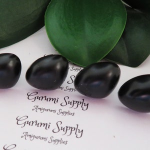 May include: Five black plastic safety eyes for amigurumi projects. The eyes are oval shaped and have a glossy finish.
