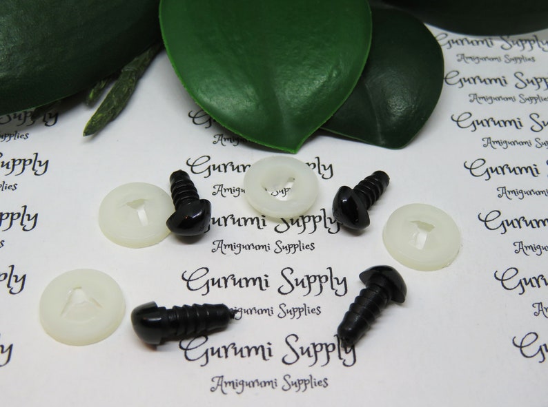 May include: Black plastic safety eyes with white plastic washers. The eyes are on a white surface with the text "Gurumi Supply Amigurumi Supplies" printed on it.
