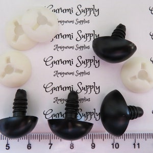 May include: Close-up of black and white plastic safety eyes for amigurumi projects. The eyes are 12mm in diameter and have a screw-on back. The image shows the eyes next to a ruler, with the text "Gurumi Supply" printed on the background.