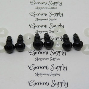 May include: A close-up of eight black plastic safety eyes with screw backs. The eyes are arranged in two rows of four. The eyes are on a white background with the text "Gurumi Supply" printed on it.