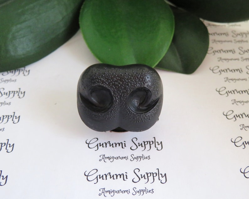 May include: Black plastic amigurumi nose with a textured surface and two small holes for nostrils. The nose is approximately 1 inch in diameter.