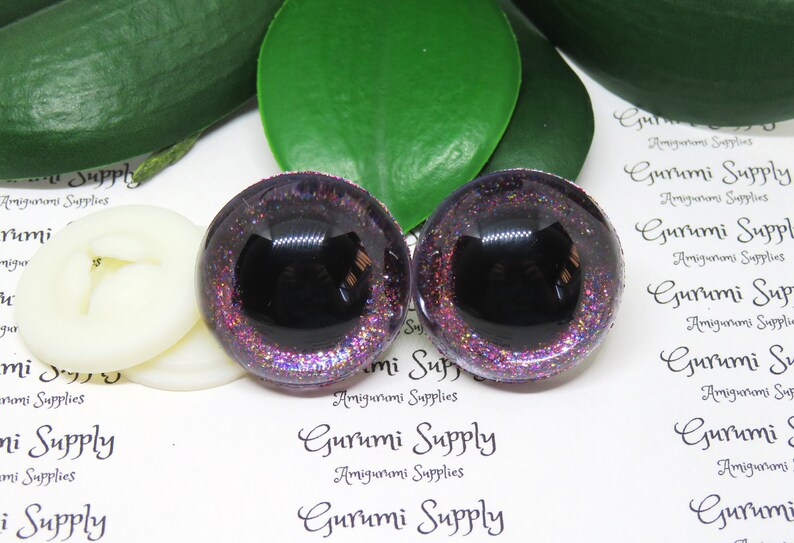 May include: Pair of black and purple glitter safety eyes for amigurumi projects. The eyes have a black pupil and a purple glitter surrounding the pupil. The eyes are 12mm in diameter.
