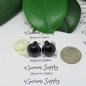 May include: Two black plastic safety eyes for amigurumi projects, next to a white button and a US dime for size comparison. The eyes are 12mm in diameter. The image includes the text "Gurumi Supply Amigurumi Supplies".