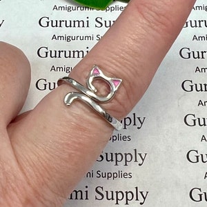 Może przedstawiać: Srebrny, regulowany pierścionek z motywem kota. Uszy kota są różowe.