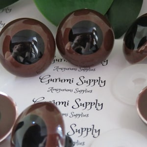 May include: Five brown plastic safety eyes with black pupils. The eyes are various sizes and some have a black plastic washer behind them.