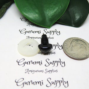 May include: Black plastic safety eyes with a screw back and a white plastic washer. The eyes are shown next to a US dime for size comparison. Gurumi Supply is printed on the white background.