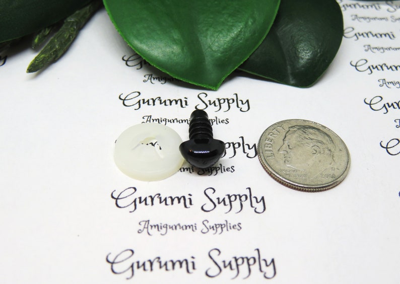 May include: Black plastic safety eyes with a screw back and a white plastic washer. The eyes are shown next to a US dime for size comparison. Gurumi Supply is printed on the white background.