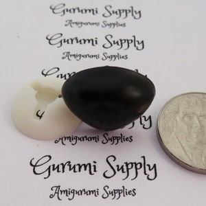May include: A close-up of a black plastic safety eye for amigurumi projects. The eye is about the size of a US quarter.