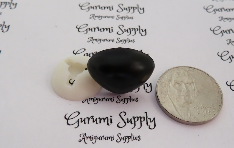 May include: A close-up of a black plastic safety eye for amigurumi projects. The eye is about the size of a US quarter.