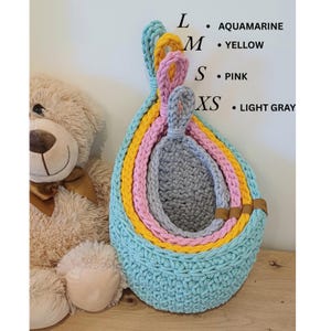 K&ouml;nnte beinhalten: Set aus vier geh&auml;kelten H&auml;ngek&ouml;rben in Aqua, Gelb, Rosa und Hellgrau. Die K&ouml;rbe sind ineinander verschachtelt, wobei der gr&ouml;&szlig;te Korb unten und der kleinste oben ist. Die K&ouml;rbe sind aus einem dicken, strukturierten Garn gefertigt.