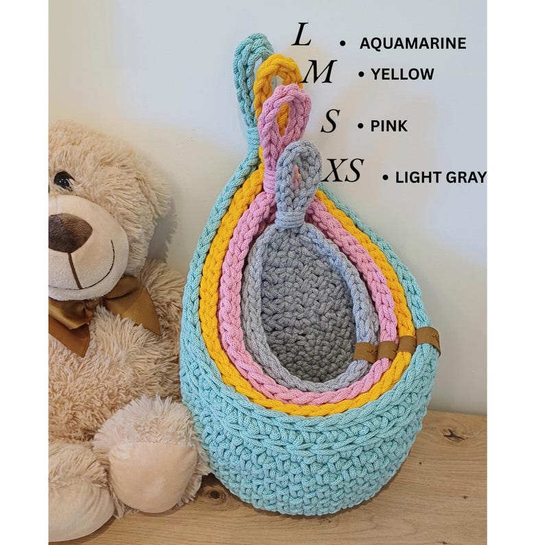 K&ouml;nnte beinhalten: Set aus vier geh&auml;kelten H&auml;ngek&ouml;rben in Aqua, Gelb, Rosa und Hellgrau. Die K&ouml;rbe sind ineinander verschachtelt, wobei der gr&ouml;&szlig;te Korb unten und der kleinste oben ist. Die K&ouml;rbe sind aus einem dicken, strukturierten Garn gefertigt.
