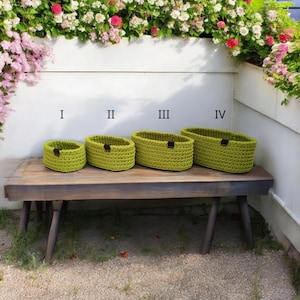 Peut inclure: Quatre paniers ovales en crochet vert de diff&eacute;rentes tailles, &eacute;tiquet&eacute;s I, II, III et IV, pos&eacute;s sur un banc en bois.