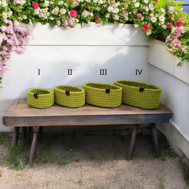 Peut inclure: Quatre paniers ovales en crochet vert de diff&eacute;rentes tailles, &eacute;tiquet&eacute;s I, II, III et IV, pos&eacute;s sur un banc en bois.