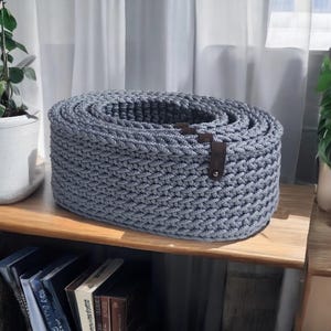 Peut inclure: Un panier de rangement ovale en crochet gris avec une poign&eacute;e en cuir. Le panier est fait d'une corde &eacute;paisse et a un motif tiss&eacute;.