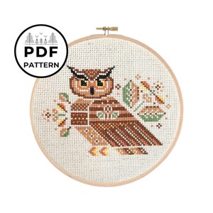 May include: A cross-stitch pattern of an owl with brown, orange, and yellow feathers, surrounded by stylised leaves and flowers. The pattern is in a round embroidery hoop.