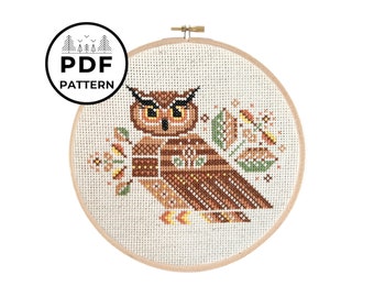 May include: A cross-stitch pattern of an owl with brown, orange, and yellow feathers, surrounded by stylized leaves and flowers. The pattern is in a round embroidery hoop.