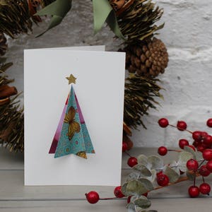 Tarjeta navideña en 3D. Árbol de Navidad de estilo escandinavo hecho a mano, hecho con papel plegado. Rosa, azul, dorado y blanco.