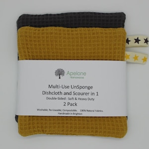 Könnte beinhalten: Zwei Mehrzweck-Geschirrtücher, eines grau und eines gelb, mit einem Etikett mit der Aufschrift "Multi-Use UnSponge Dishcloth and Scourer in 1 Double-Sided: Soft & Heavy Duty 2 Pack Washable; Re-Useable: Compostable. 100% Natural Fabrics. Handmade in Brighton"